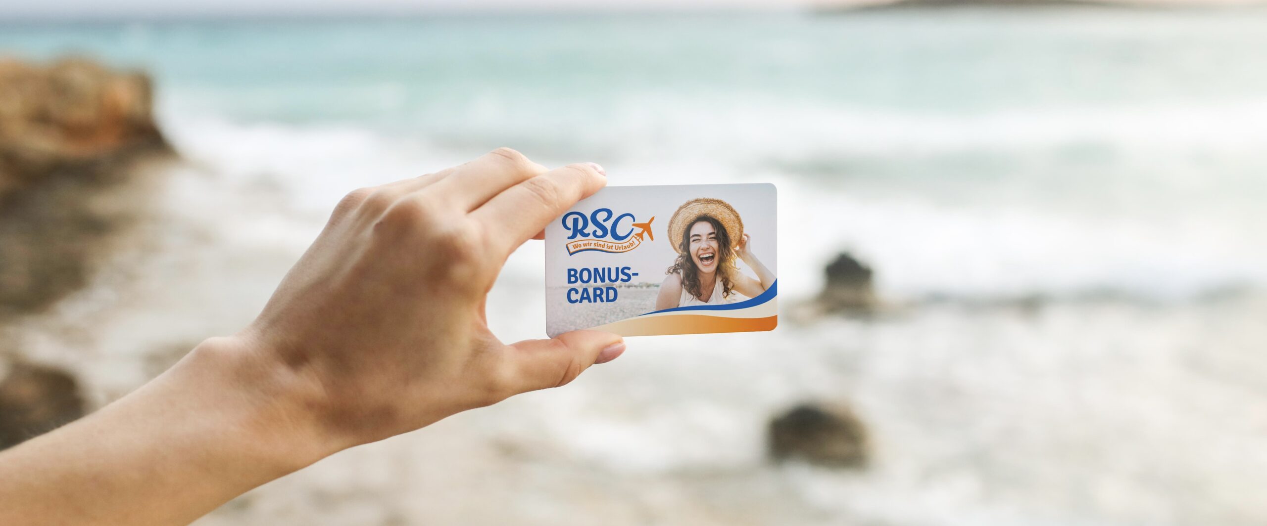 female hand is holding a white business card or sticky note with place for text on the beach background and the sea making waves. selective focus.